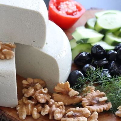 Wooden dish with sunflower seed tofu or vegan white cheese, tomato, cucumber, and walnuts