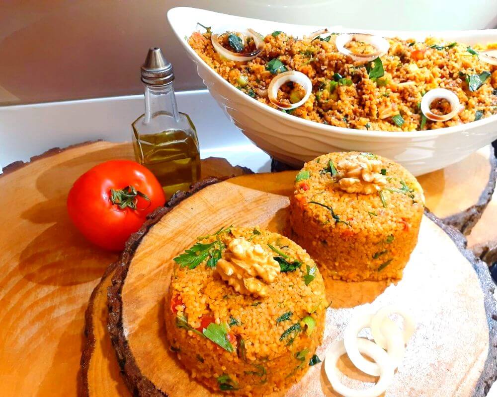 A bowl of Turkish Bulgur Salad (Kisir) garnished with fresh lemon and a side of pita bread or crackers.
